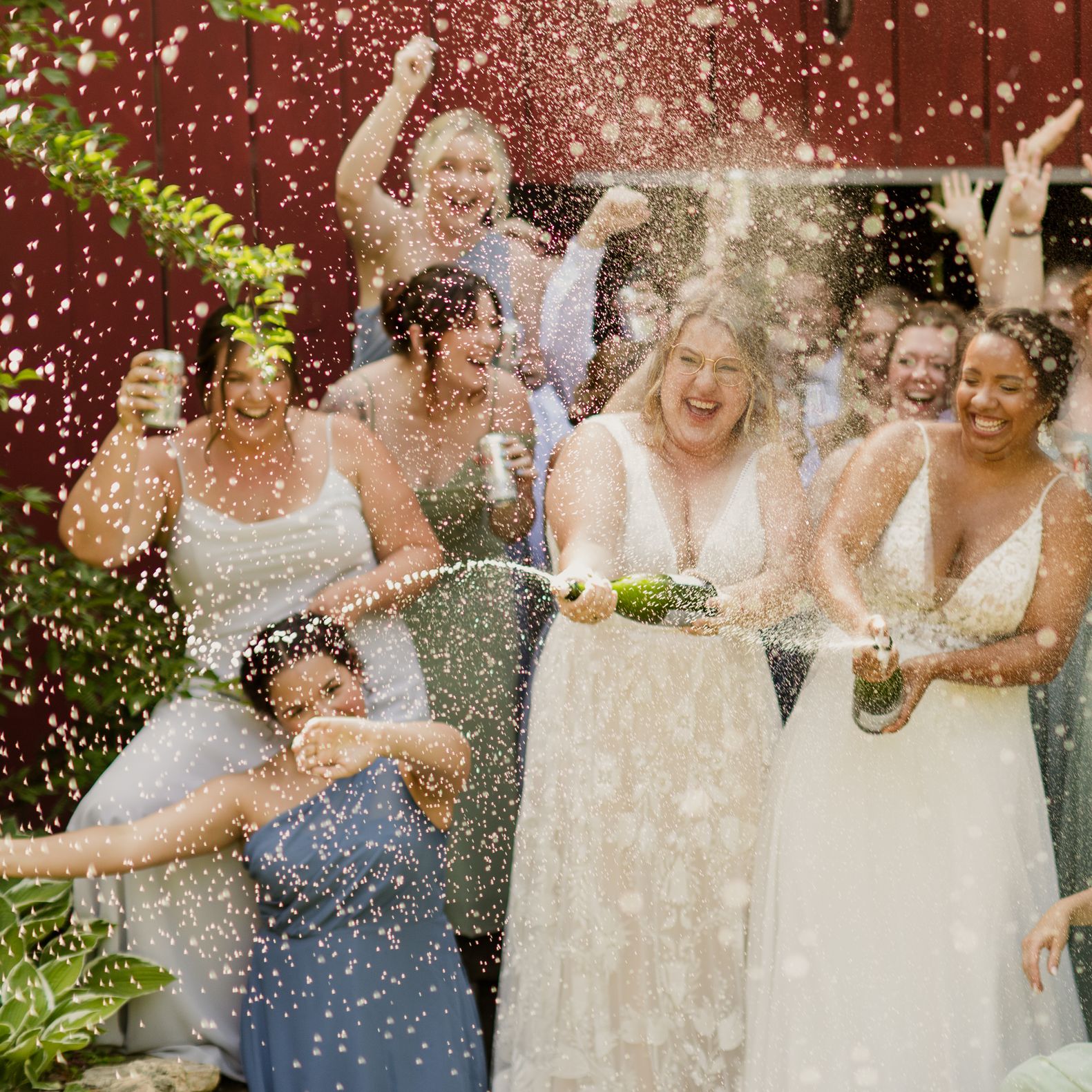 Brides spray champagne bottle surrounded by their bridal party