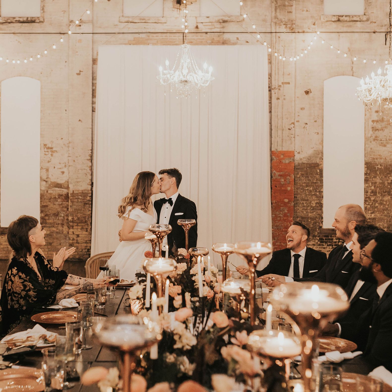 Madison and Robert Share a Kiss at the Head of their Table in Modern Industrial Wedding at Northern Pacific Center