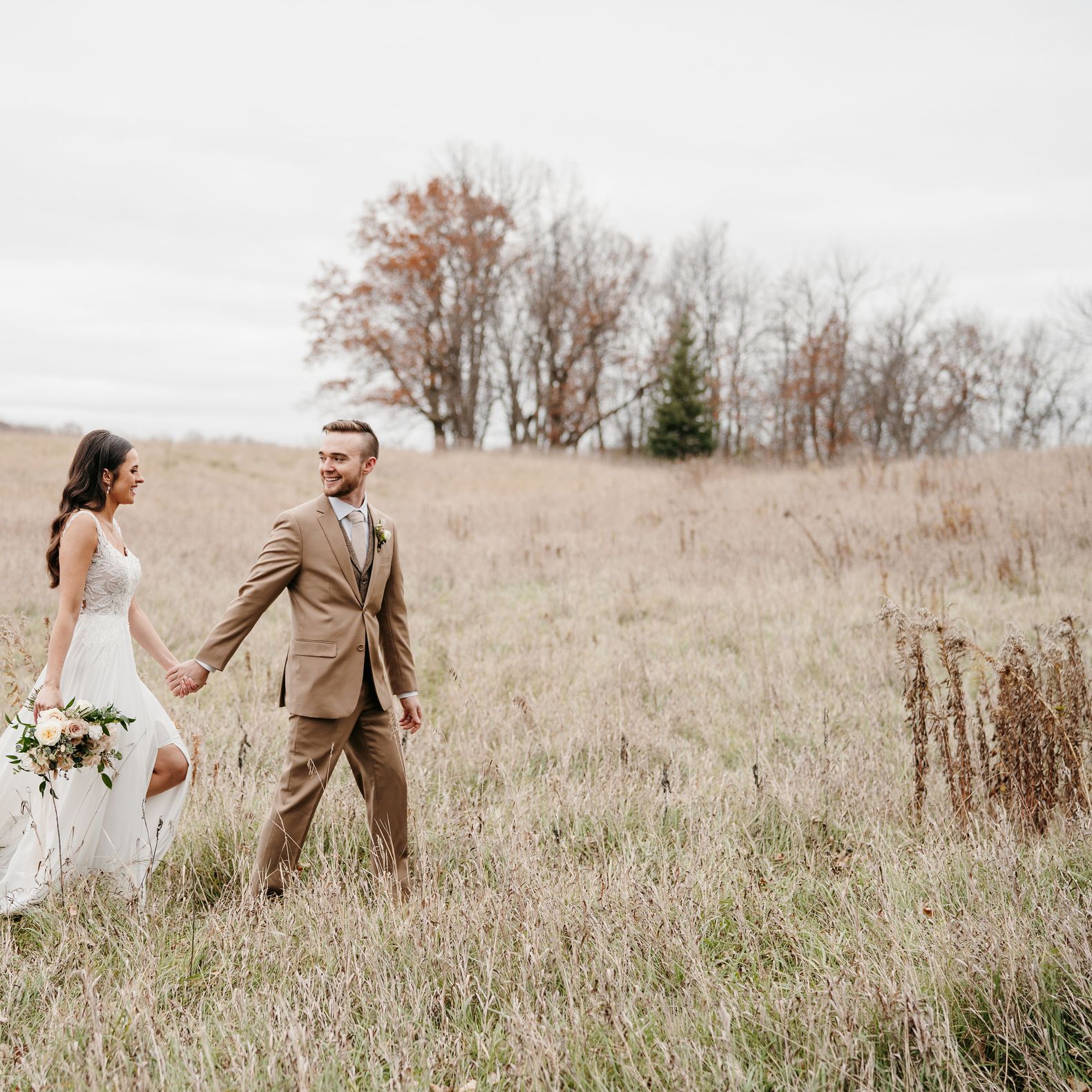 Maddie and Josh Walk Hand in Hand Through a Muted Grass Field at Creekside Farm