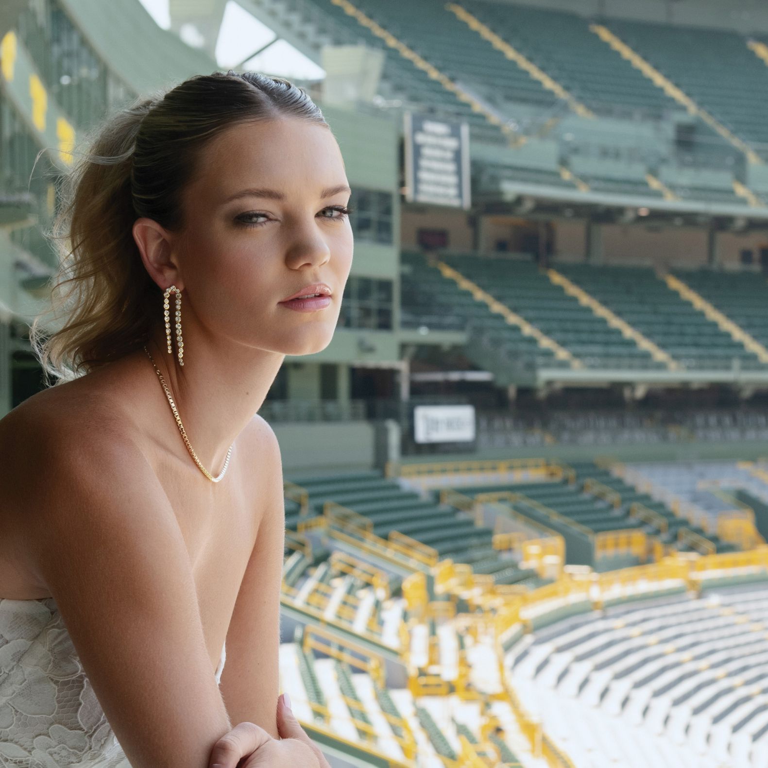 Model poses in bridal attire and jewelry looking over Lambeau Field