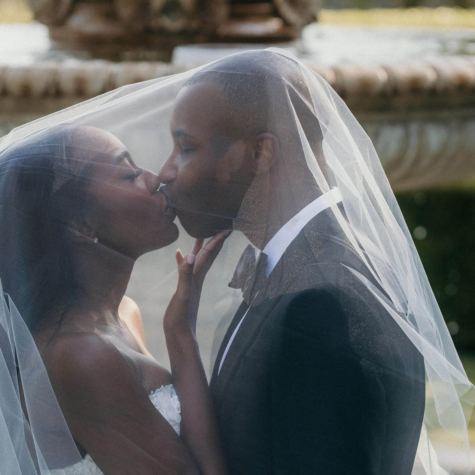 Bride and groom kiss under bride's veil in front of a fountain at Greystone Mansion
