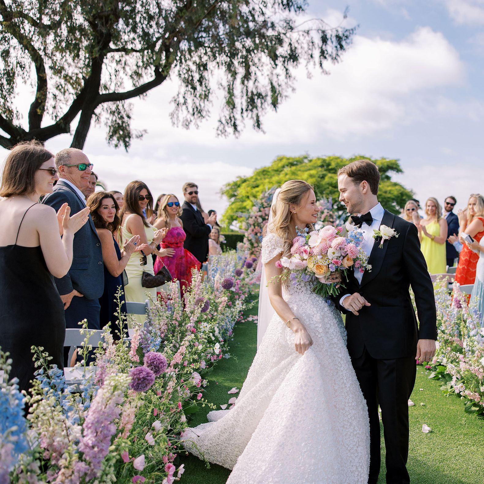 Bride and groom walk back down outdoor floral lined aisle after getting married at La Jolla Country Club