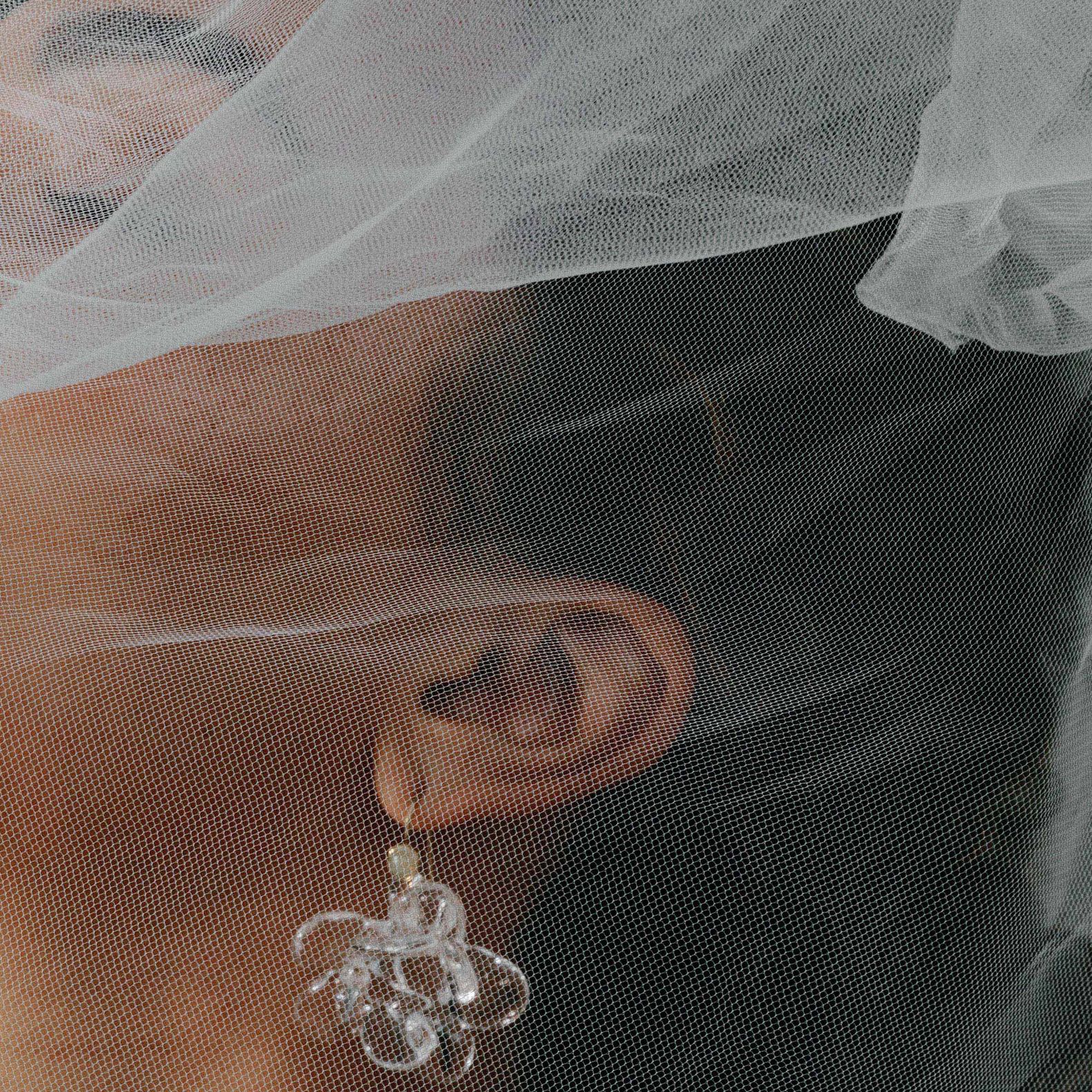 Model poses with holding veil over her face, showcasing stunning accessories in editorial shoot