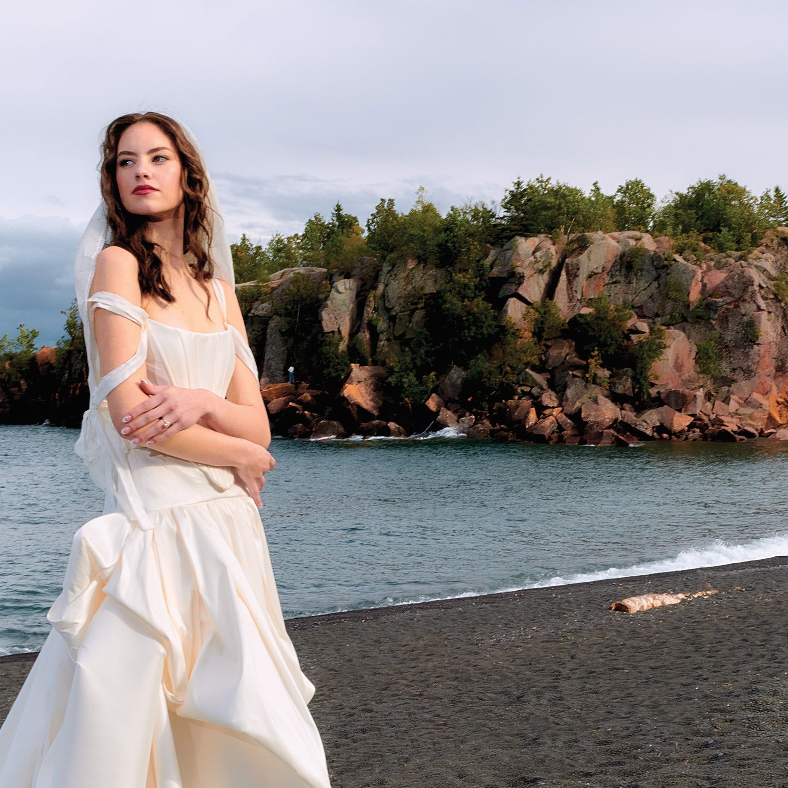 Model poses in fashion-forward wedding gown on the Black Sand Beach with Lake Superior in the background