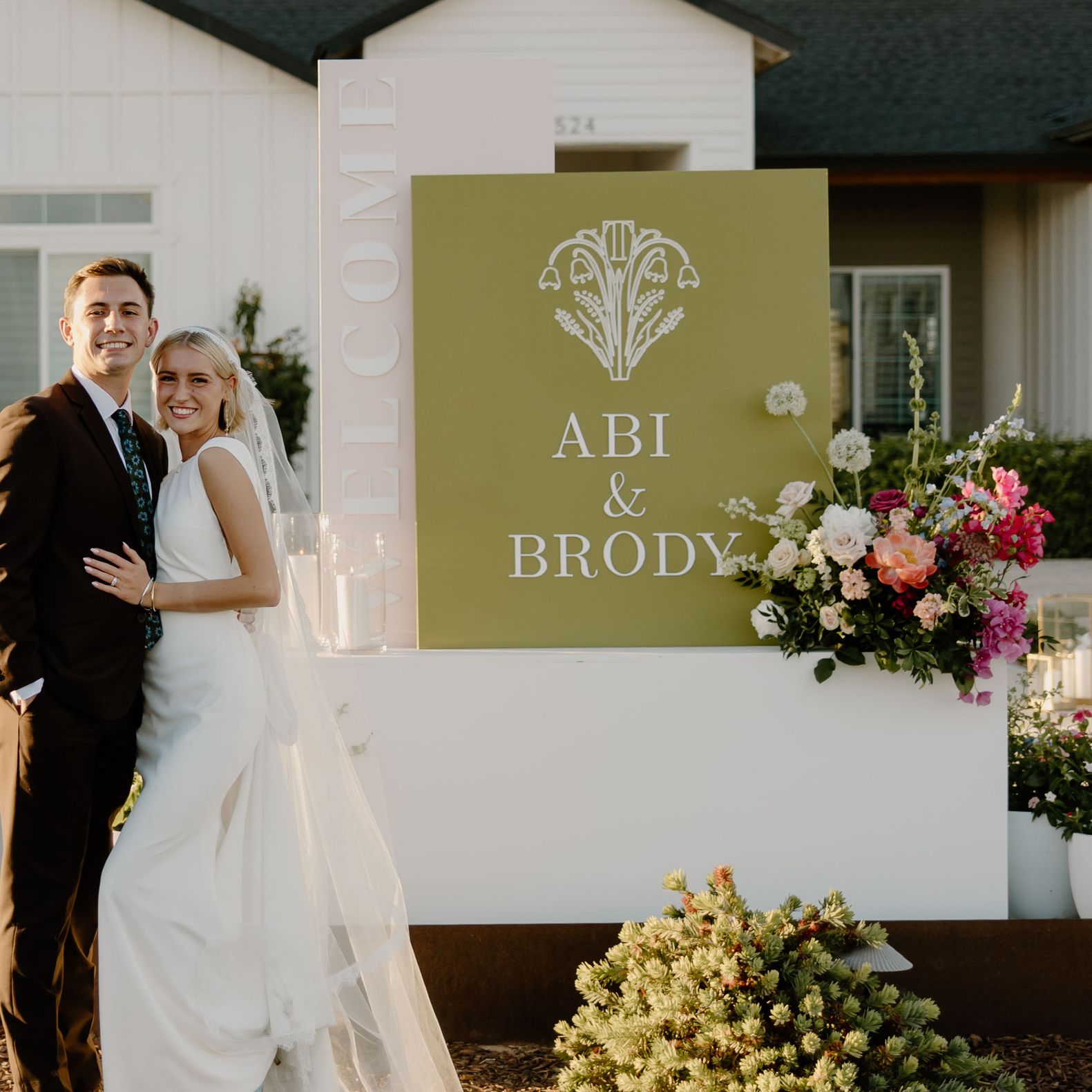 Bride and groom pose in front of groom's house, vintage getaway car and welcome sign