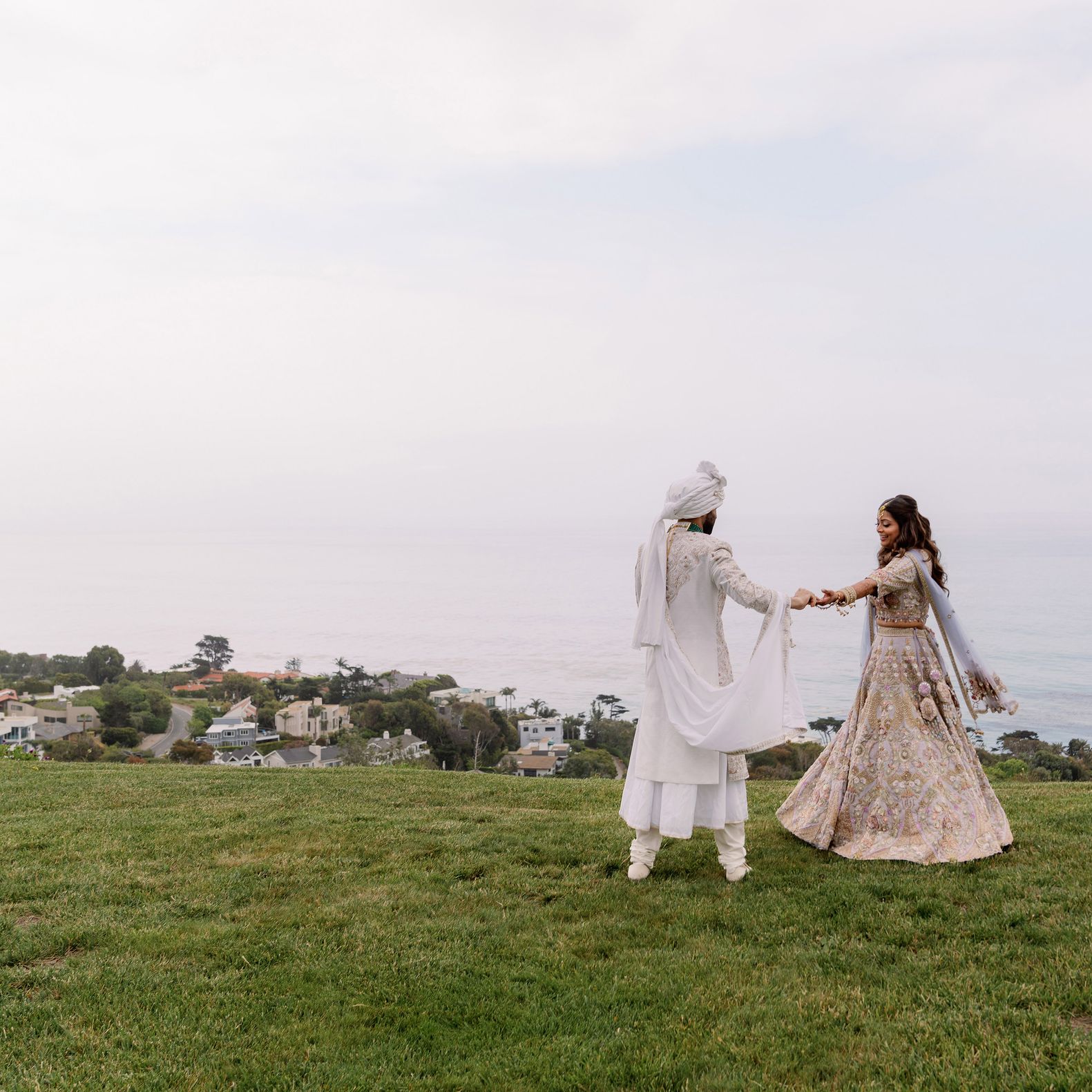 Bride and groom stand hand in hand with the misty coastline in the background