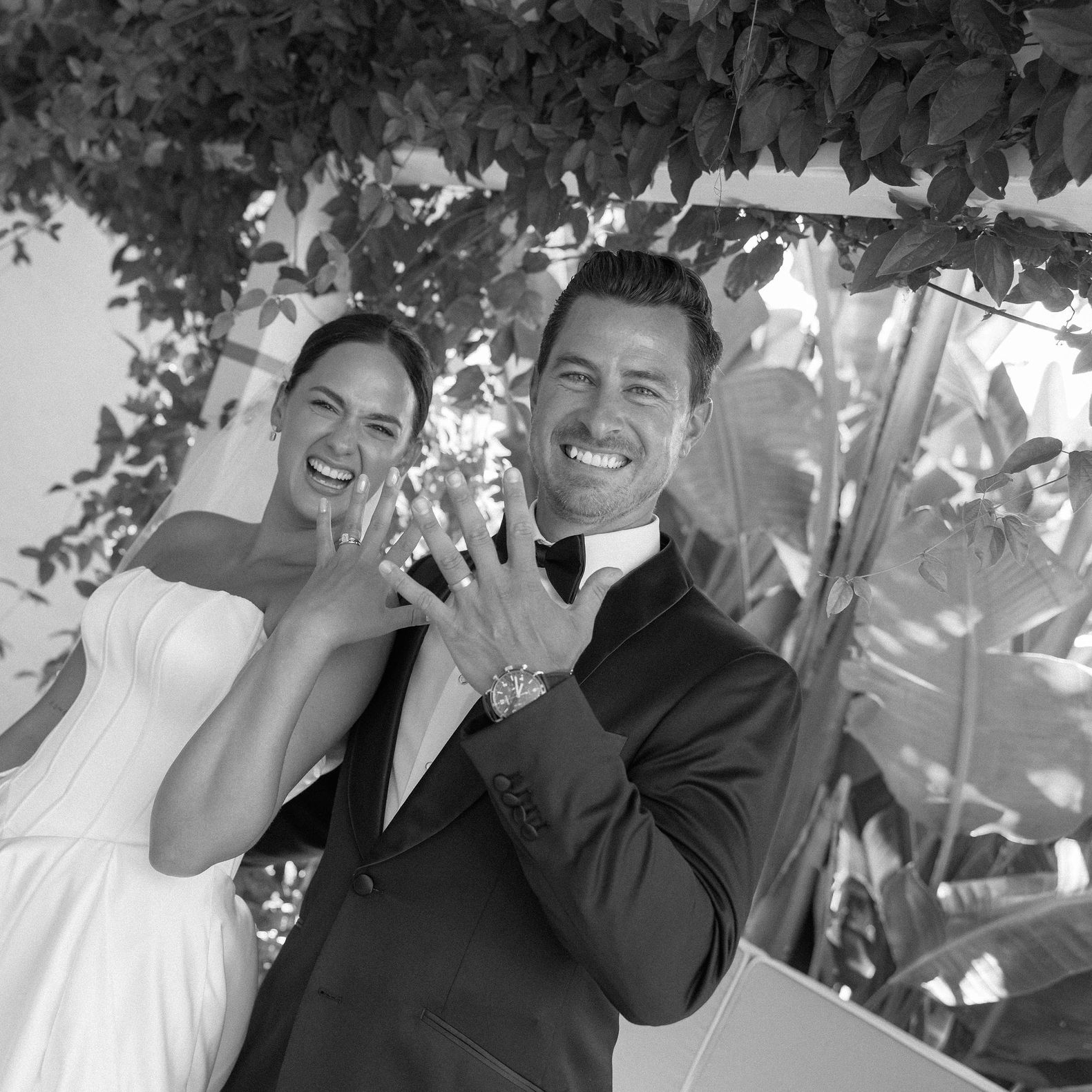 Bride and groom smile with their hands raise to show off their rings and newlywed status