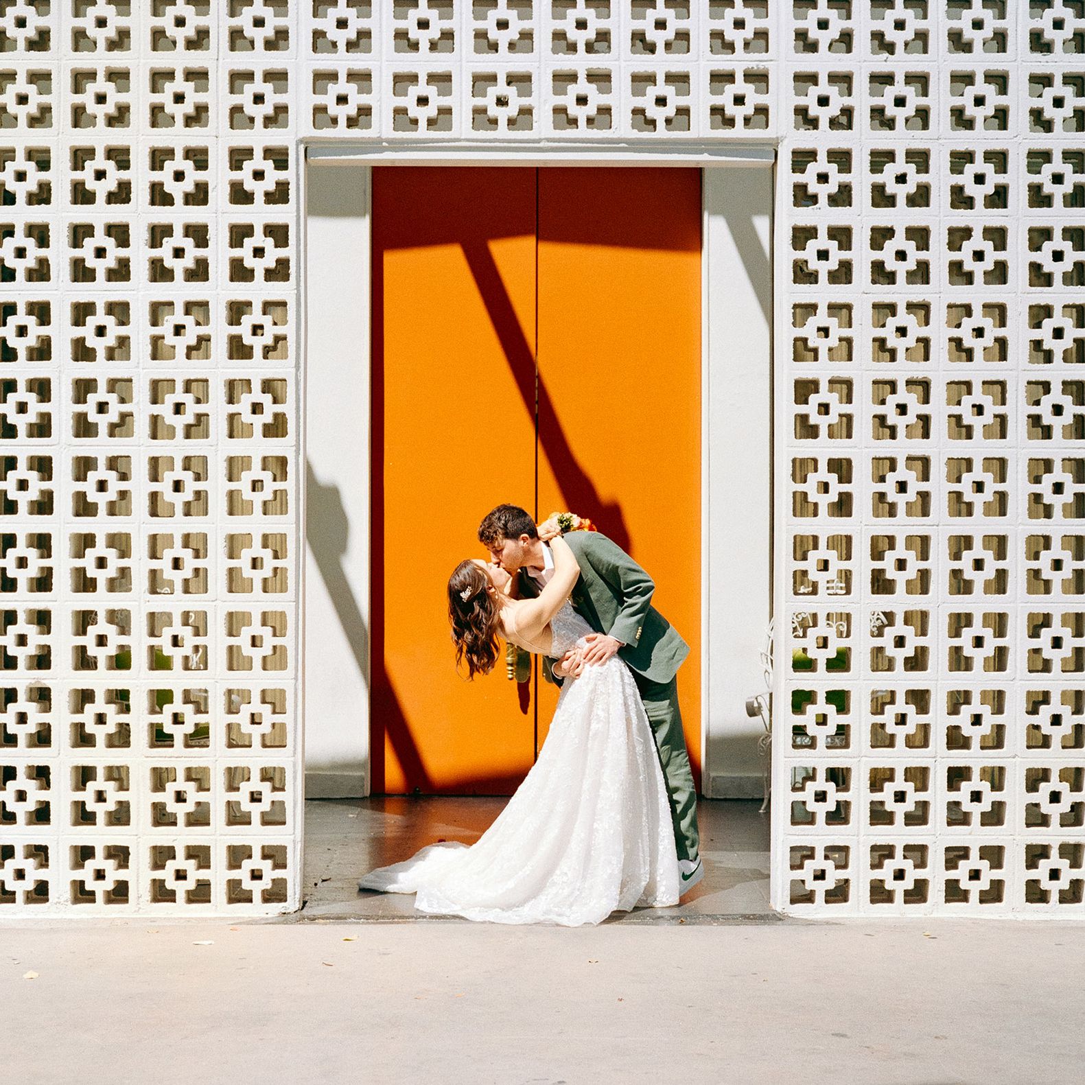 Bride and groom share a kiss against orange door in wedding day at Parker Palm Springs 