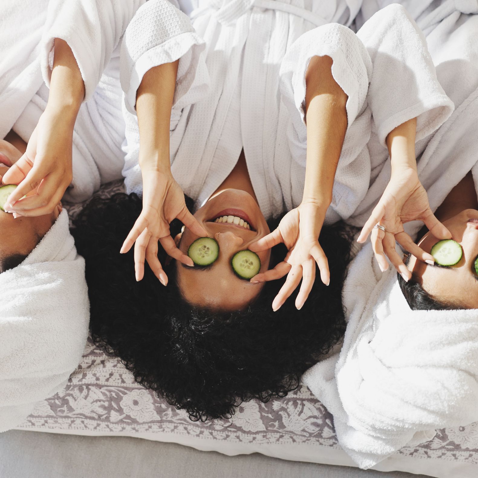 Bridesmaids in white robes relaxing during a wellness-focused bachelorette party with cucumber eye masks and spa treatments