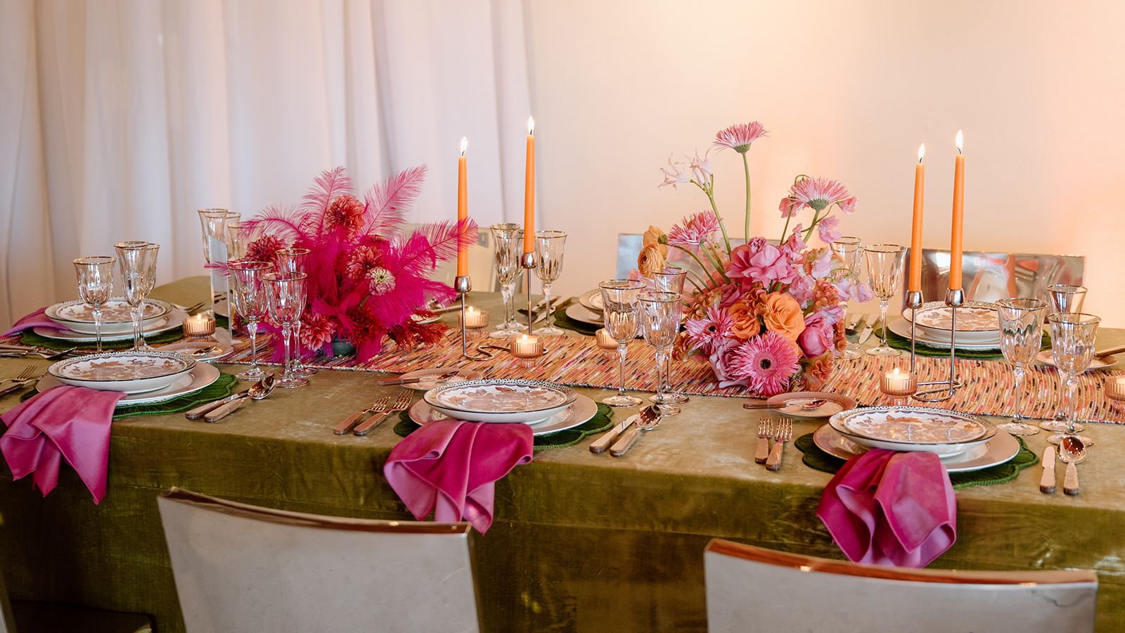 Colorful maximalist wedding tablescape with pink and orange floral centerpieces, green velvet linens and orange taper candles