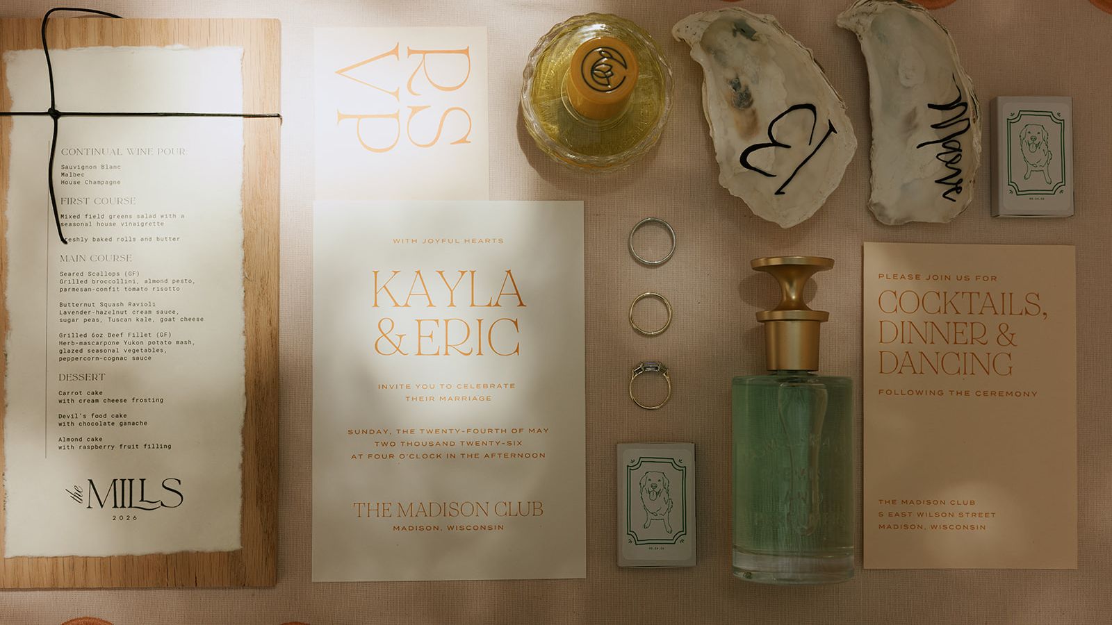 Flat lay of wedding invitations, a menu, rings, perfume and illustrated details for Kayla and Eric’s Madison Club celebration.