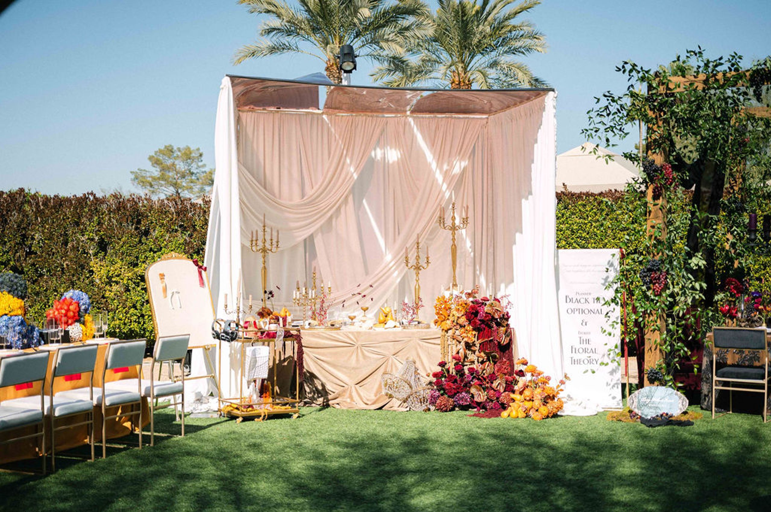 Elegant wedding table setup with draped fabric, gold candelabras, lush floral arrangements, and an interactive station featuring headphones and a writing station with ribbons.