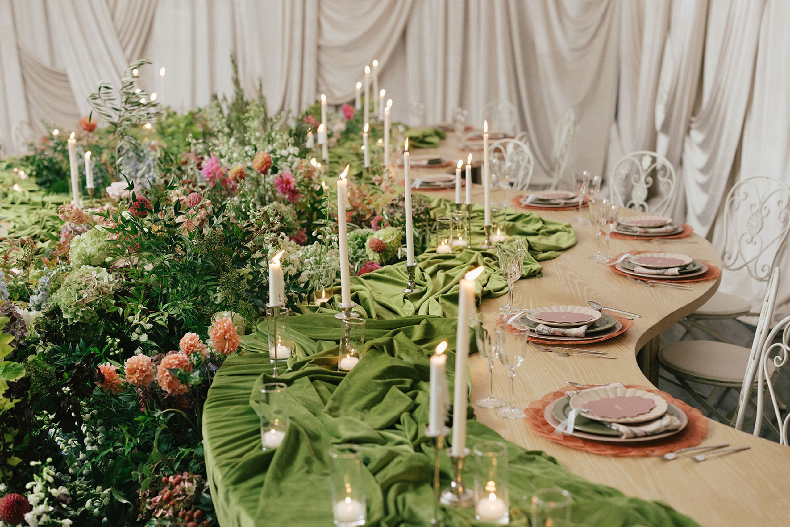Serpentine tablescape featuring vivid décor, bright florals and romantic candlelight set against a draped background in editorial at The Woodland