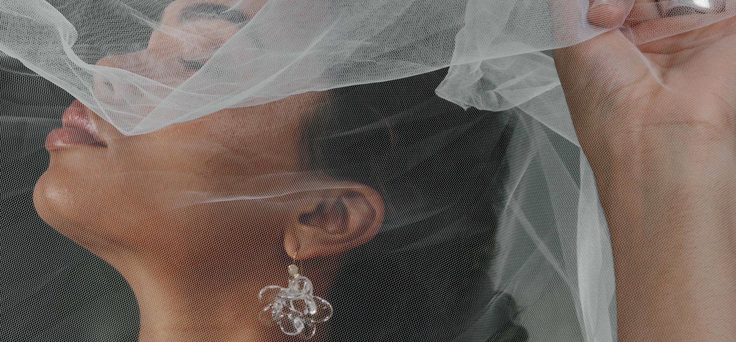Model poses with holding veil over her face, showcasing stunning accessories in editorial shoot