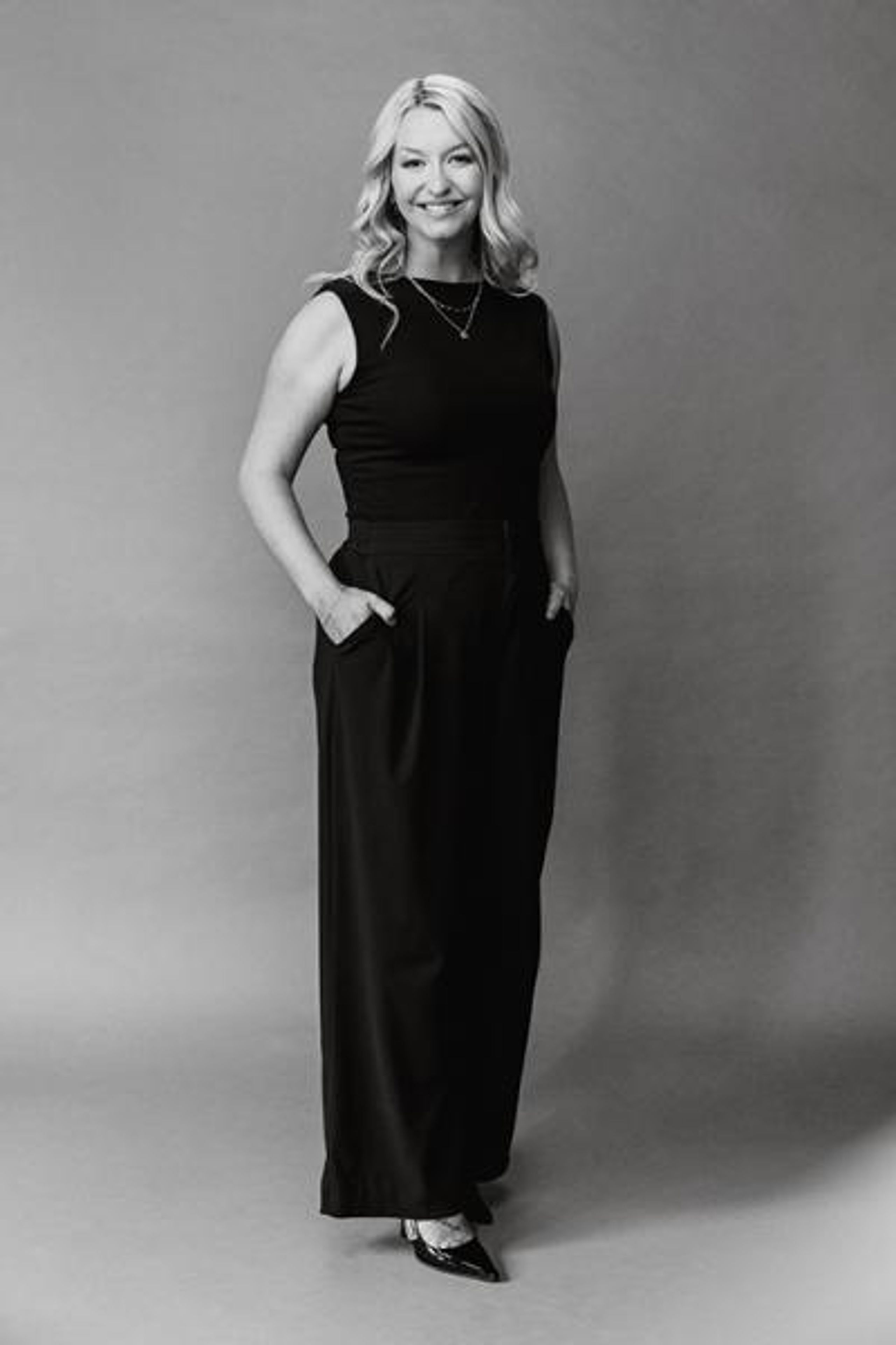 Headshot of Arizona Bride publisher Brittany O'Neill, standing wearing all black, smiling with hands in pockets