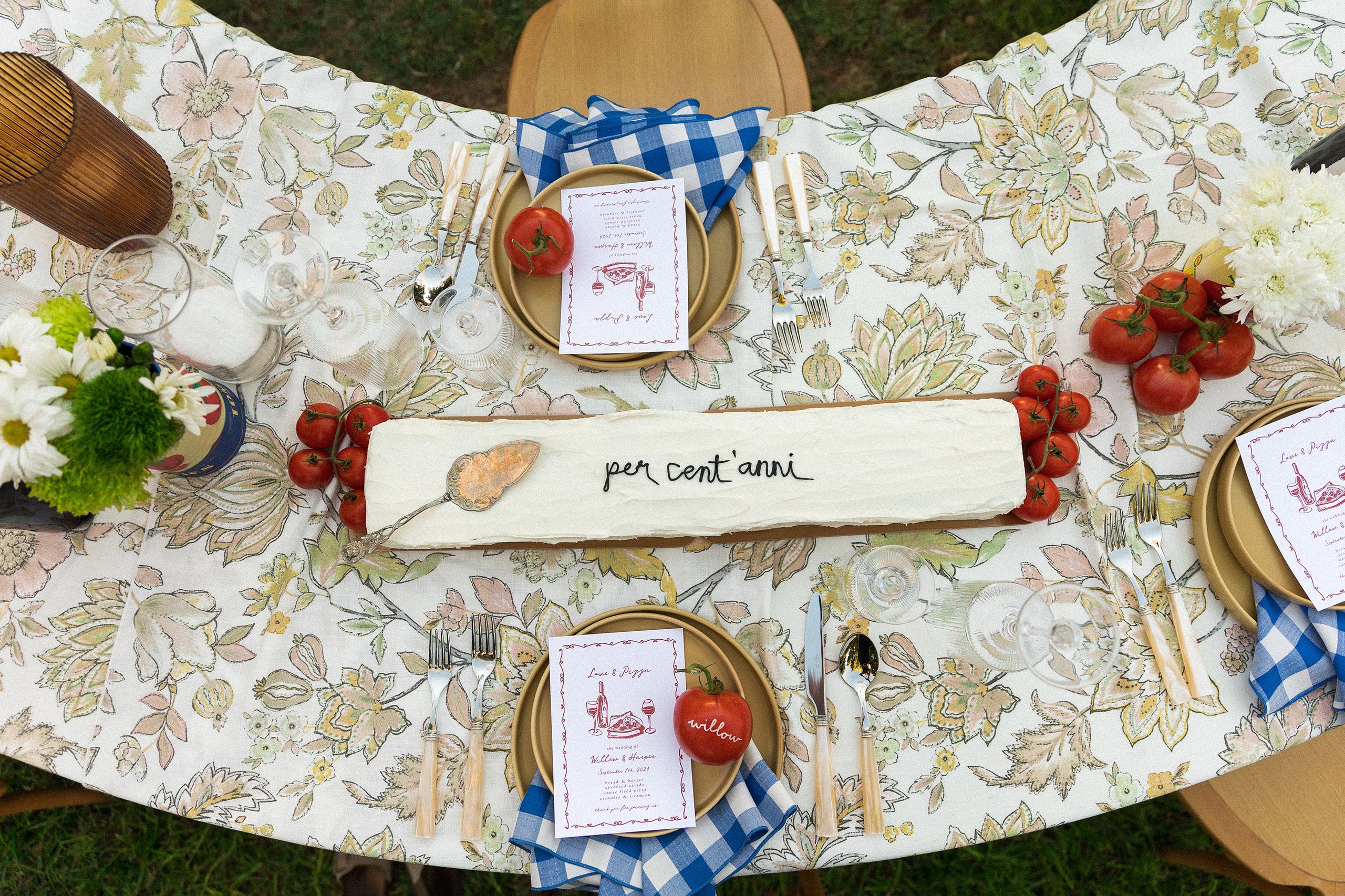 Horizontal cake with "per cent'anni" written in frosting on Italian-inspired tablescape featuring tomatoes as décor