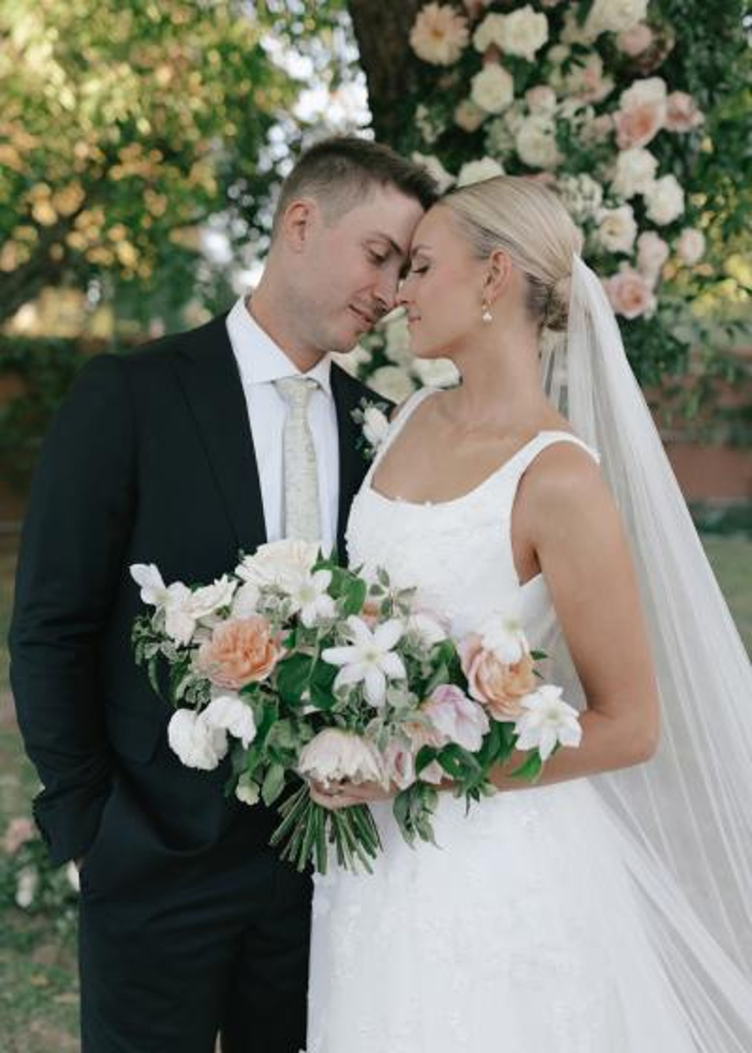 Bride and groom stand with foreheads pressed together, the bride holding her bouquet at their outdoor wedding day