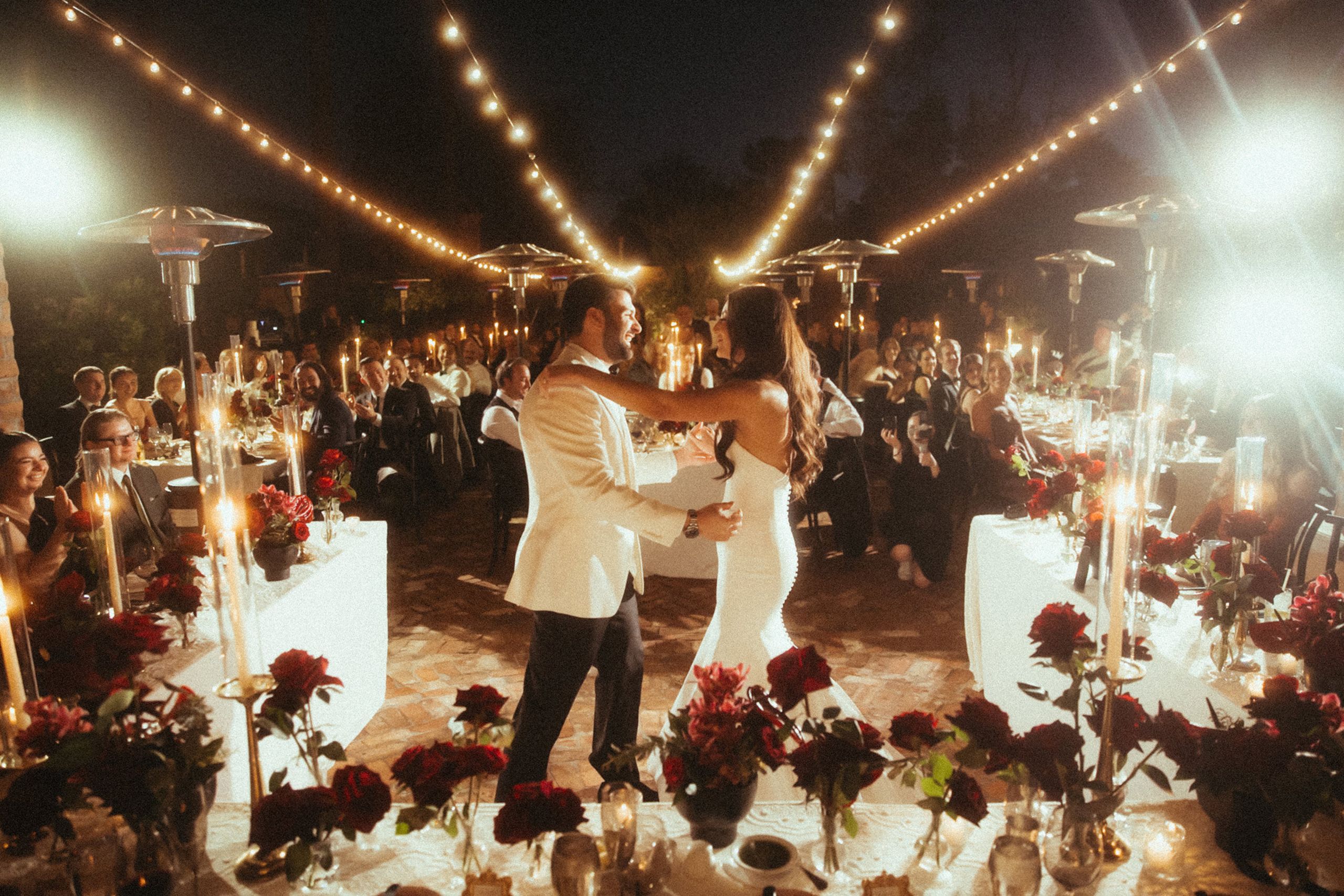 Bride and groom share a dance framed by their candlelit outdoor reception featuring bold red flowers at Royal Palms Resort and Spa