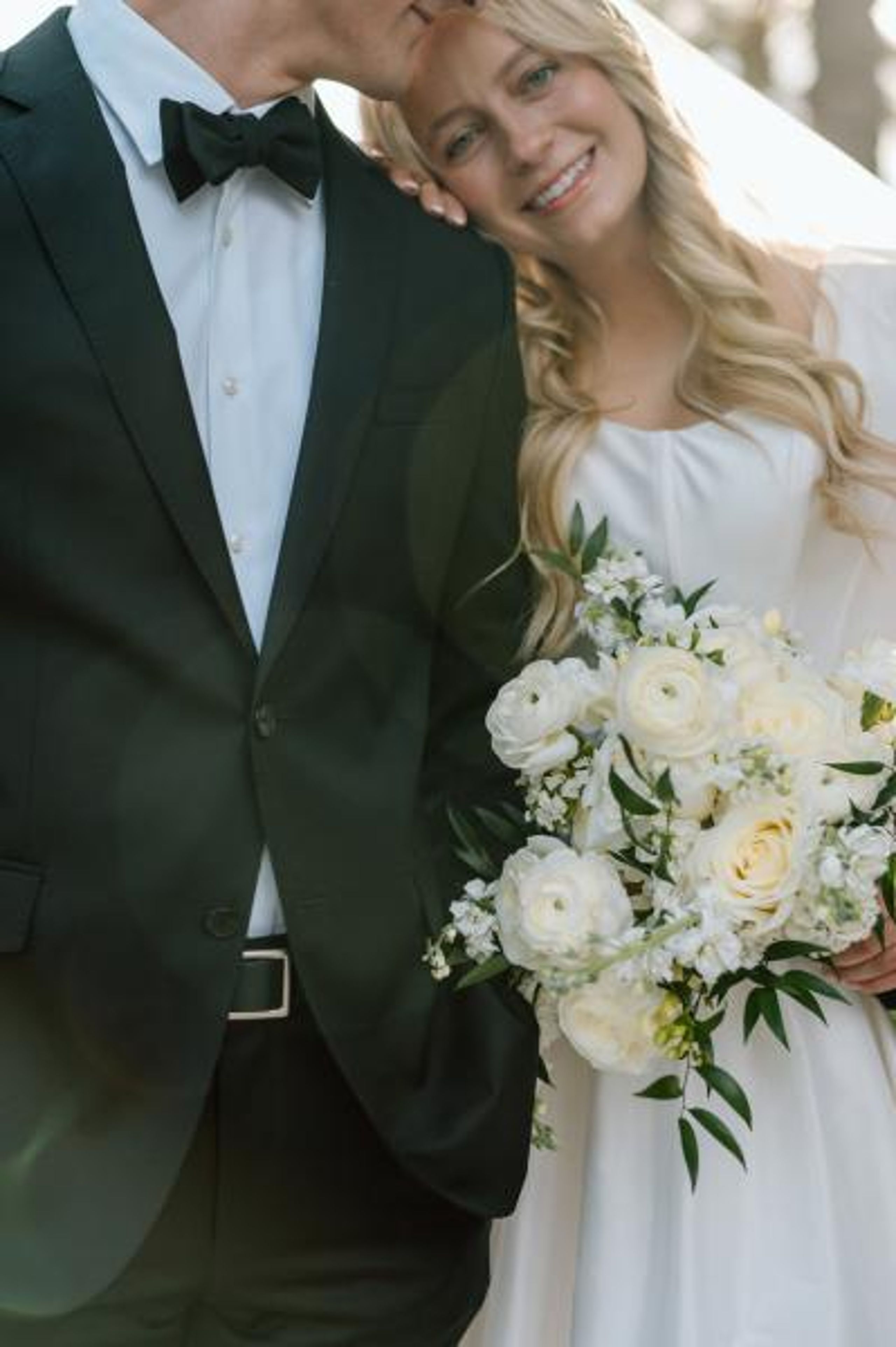 Bride rests her head on groom's shoulder, bouquet in hand on their wedding day at a family farm