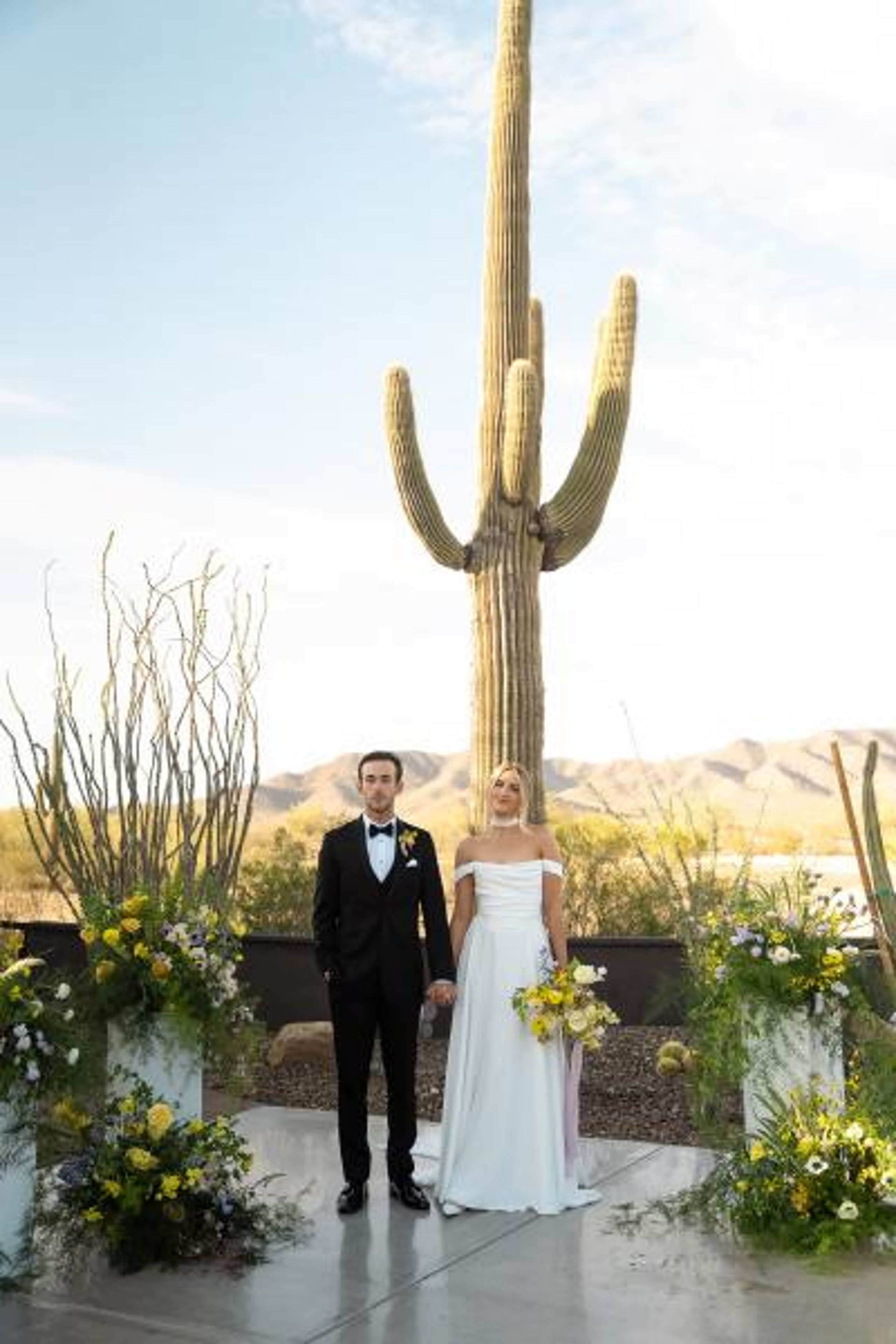 Bride and groom stand hand in hand at the altar, framed by bright blooms and cacti at The Willow Weddings & Event Center