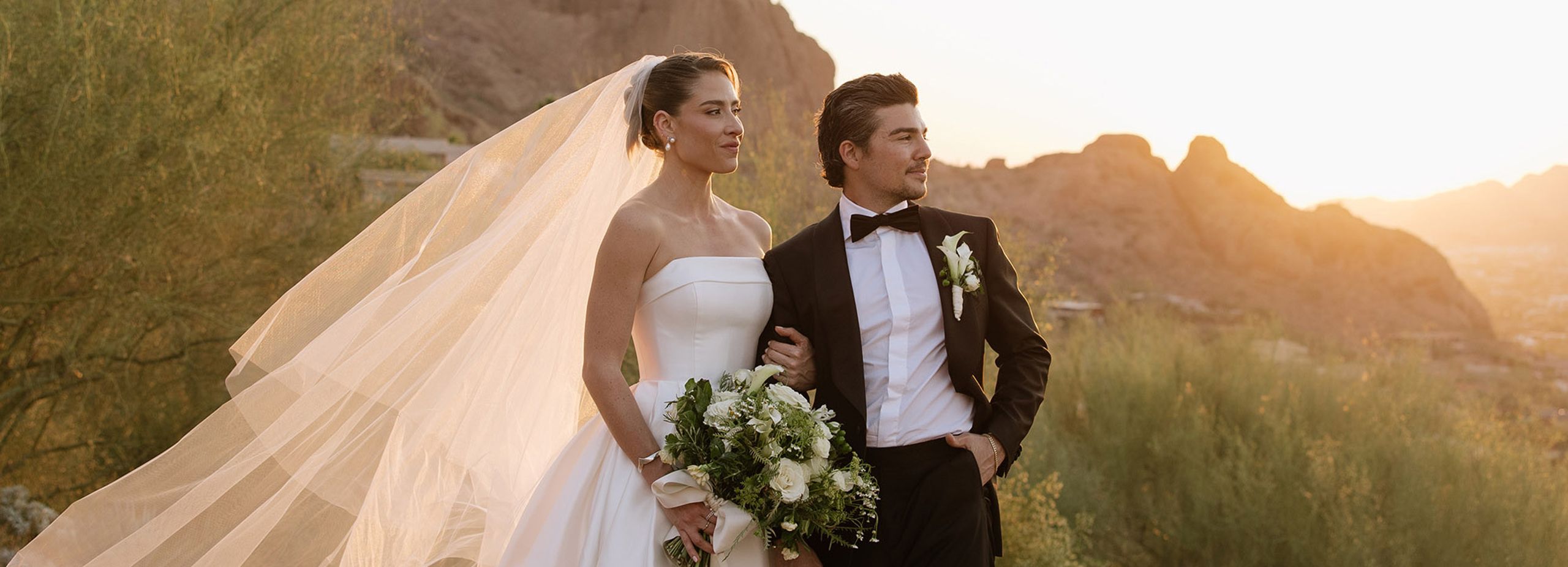 Bride and groom pose on the rocks of Camelback Mountain with the golden hour casting a glow behind them