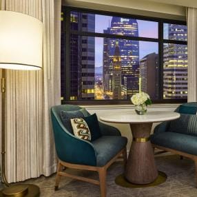 Cozy up in the stylish queen room sitting area at the Ritz-Carlton, Denver, showcasing plush teal chairs and a stunning cityscape view, perfect for a relaxing evening or intimate gathering