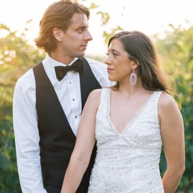 Bride and groom pose in their after party outfits with sunlit greenery in the background