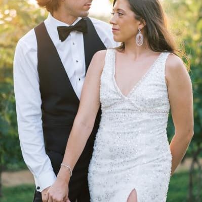 Bride and groom pose in their after party outfits with sunlit greenery in the background