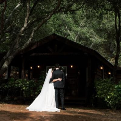Bride and groom pose, shaded by dark trees on the grounds of Villa Loriana