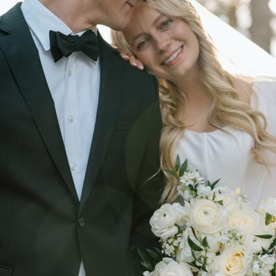 Bride rests her head on groom's shoulder, bouquet in hand on their wedding day at a family farm