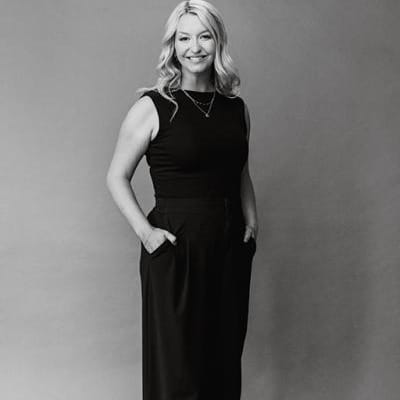Headshot of Arizona Bride publisher Brittany O'Neill, standing wearing all black, smiling with hands in pockets