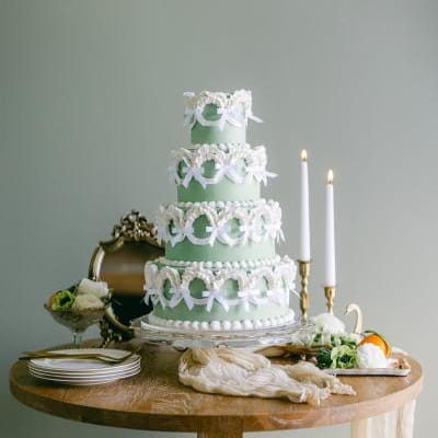 Four-tier green wedding cake in a vintage style with tiers lined with white bows