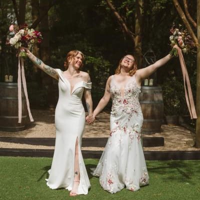 Two brides in different dresses and dark, autumnal bouquets smile after ceremony