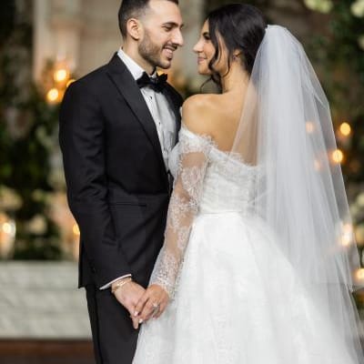 A gorgeous couple in classic wedding attire with long veil at elegant greenery altar with Armenian touches