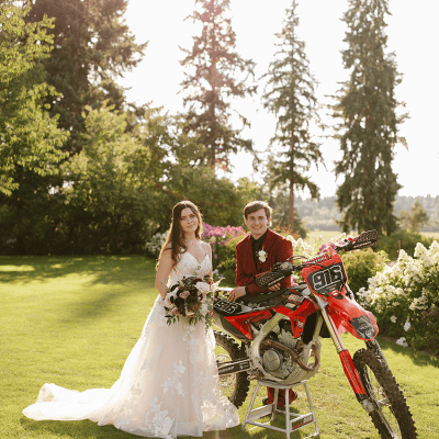 Bride with bouquet and groom in red suit pose with motocross dirt bike