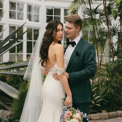Hannah Fuchigami and Gunnar Conley pose at the W.W. Seymour Botanical Conservatory before their wedding, with lush greenery and floral accents in the background