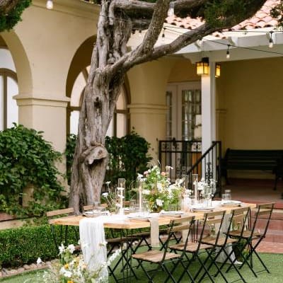 Table and chairs with nature-inspired decor and florals, underneath a large tree