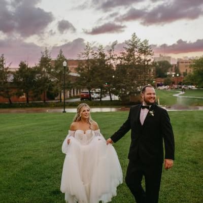 Bride and groom walk through field against a stormy sunset