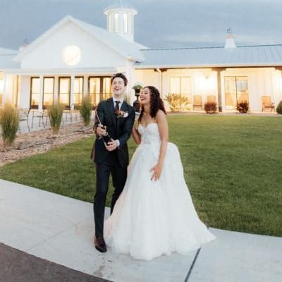 Bride and groom pop champagne in front of modern venue