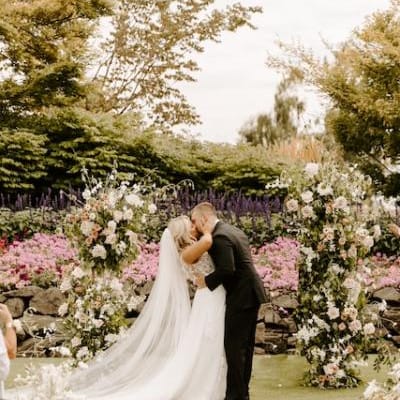 Kristin and Mason Share a Kiss in Front of Neutral Floral Arch After Exchanging Vows at Langdon Farms Golf Club