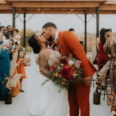 The newlyweds share a kiss down the aisle after their ceremony, with fall-inspired florals, pampas grass and joyful guests in the background.