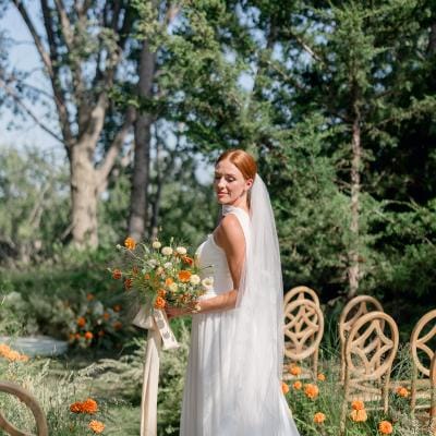 Model in simple bridal attire holding bouquet standing among the ceremony scene at Petal and Thorn Flower Farm