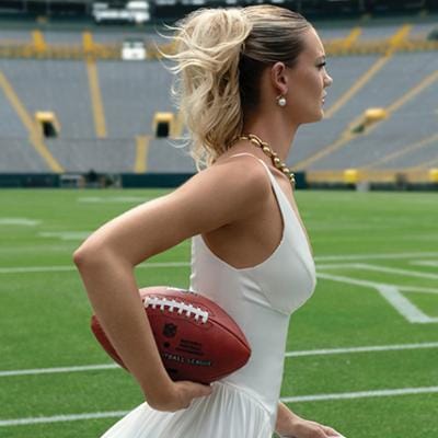 Model in bridal wear and jewelry poses running with football on Lambeau Field
