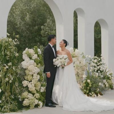 Bride and Groom smile at each other in front of modern altar surrounded by lush organic florals