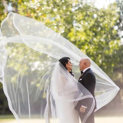 Bride and groom pose outside, the bride's veil catching on a dramatic wind