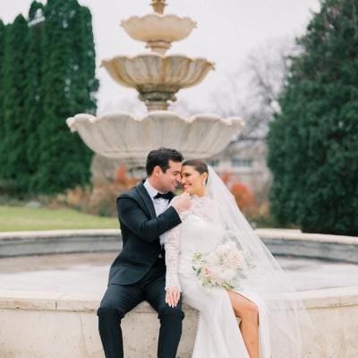 Bride and groom pose sitting at the edge of a water fountain 