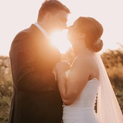 Bride and groom embrace outside at Woodland Glasshouse with the sun shining between them