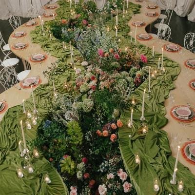Serpentine tablescape featuring vivid décor, bright florals and romantic candlelight set against a draped background in editorial at The Woodland