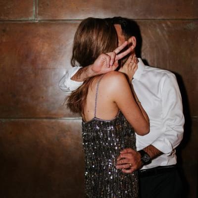 Bride and groom share a kiss in their festive after party clothes in front of a wooden wall at JM Cellars