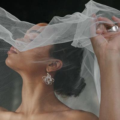 Model poses with holding veil over her face, showcasing stunning accessories in editorial shoot